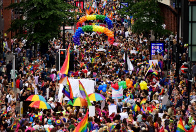 A crowd of people participating in a pride event, proudly walking down a street with rainbow flags.